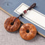 Peach Wood Bagua Coin – two carved coins with Taoist spells and Bagua symbols, brown cord bead accents, blue book backdrop, Daoist shield