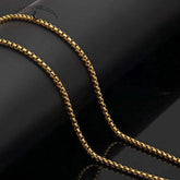 Zodiac Spin Necklace – gold box chain close up, black reflective background showing metal link detail, Buddhist necklace chain
