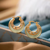 Crescent Moon Jade Drop Earrings – Gold openwork hoop earrings with white crescent-shaped jade inlay and geometric lattice cutouts on teal velvet, side angle