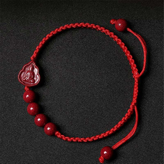 Cinnabar Laughing Buddha Guan Yin Bracelet – red cord with cinnabar beads and carved Buddha pendant, black fabric flat lay