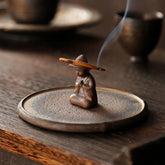Ceramic Meditating Figure Incense Burner with rising smoke on wood table, mindful