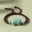 Jade PiXiu Knot Bracelet – Dark red braided cord bracelet with light green jade PiXiu on beige surface