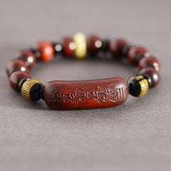 Red Sandalwood Om Bracelet – low angle on gray fabric, polished wood beads flanking mantra centerpiece, Buddhist prayer bracelet