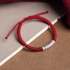 Silver Mantra Rope Bracelet – Red braided cord with silver charm on styled book and fabric setting, fortune bracelet