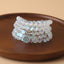 108 Mala Glitter Stone Lotus Bracelet – iridescent beads with silver lotus charm on wood dish, focused