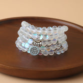 108 Mala Glitter Stone Lotus Bracelet – iridescent beads with silver lotus charm on wood dish, focused