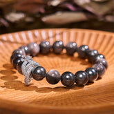 Silver Sheen Obsidian Dragon Bracelet – glossy black beads with silver dragon charm on carved wooden dish, protective energy