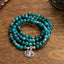 108 Mala Apatite Bracelet - coiled teal beads with Lotus Buddha charm on wooden table, zen jewelry