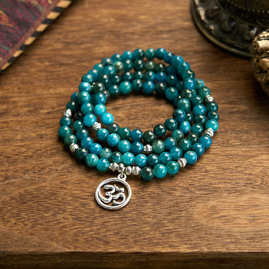 108 Mala Apatite Bracelet - coiled teal beads with Om charm on wooden table, spiritual meditation jewelry