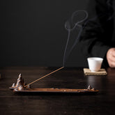 Mountains Boat Ceramic Incense Burner – brown mountain peak design with lit incense and smoke, white tea cup beside, dark moody setting