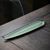 Green Bamboo Leaf Ceramic Incense Burner – light green leaf-shaped holder with incense smoke drifting on dark wood table