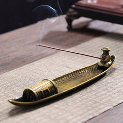 Fisherman Boat Alloy Incense Burner – angled on textured mat with trailing smoke, mindful home accent