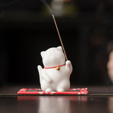 Cat Bell Ceramic Incense Burner – White cat with red bell collar holding lit incense, smoke rising, ceramic incense burner