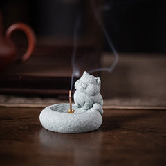 Lazy Cat Sandstone Incense Burner – seated cat with brass holder on dark wood, teapot in background, meditation accessory