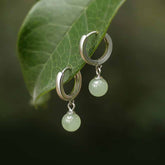 Round Jade Bead Prosperity Earrings – silver hoop with mint green jade drop on fresh green leaf, botanical natural setting