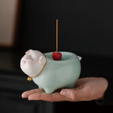 Ceramic Little Pig Incense Burner – Celadon green pig with gold bell collar, red holder on palm