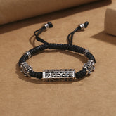 Tibetan PiXiu Bracelet – Black braided cord with silver PiXiu and copper Om Mani Padme Hum cylinder on brown paper