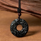 Black-green jade PiXiu peace buckle pendant on cord against brown wood