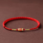 Koi Fish Braided Red String Bracelet – red cord with gold koi charm and beads, side view on brown, luck jewelry