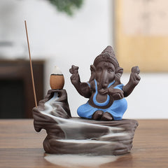 Ganesh Backflow Incense Burner - Seated deity in terracotta with blue garments, smoke cascading down, protection symbol