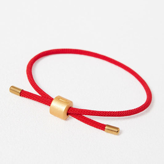 Adjustable red braided cord bracelet with gold cylindrical slider bead and end caps, minimalist lucky string jewelry on white background