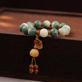 Bodhi Seed Zakiram Bracelet - Curved on dark wood showing carved green beads and Buddha pendant, beaded mala bracelet