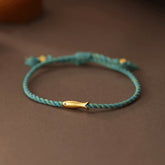 Copper Lucky Koi Fish Rope Bracelet – teal braided cord with gold koi charm on wood, luck jewelry
