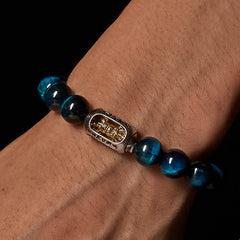 Blue Tiger Eye Om Bracelet worn on wrist - black background, mantra charm with gold deity figure, mens spiritual bead bracelet