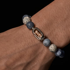 Sodalite Grey Jasper Om Bracelet – worn on wrist, dramatic lighting, blue stones with gold charm, mens spiritual jewelry