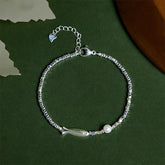 Silver Koi Fish Pearl Luck Bracelet – top-down flat-lay, koi charm and pearl on beaded chain, dark green bg