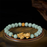 Golden Pi Xiu Charm Jade Prosperity Beaded Bracelet – Green jade bracelet with gold Pi Xiu on ceramic plate, side view