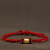 999 Gold Om Mani Padme Hum Red String Bracelet – braided red cord with gold mantra bead on neutral textured surface, red string bracelet