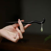 Hand holding curved ebony wood hairpin with 925 silver chain and Hetian jade teardrop pendant