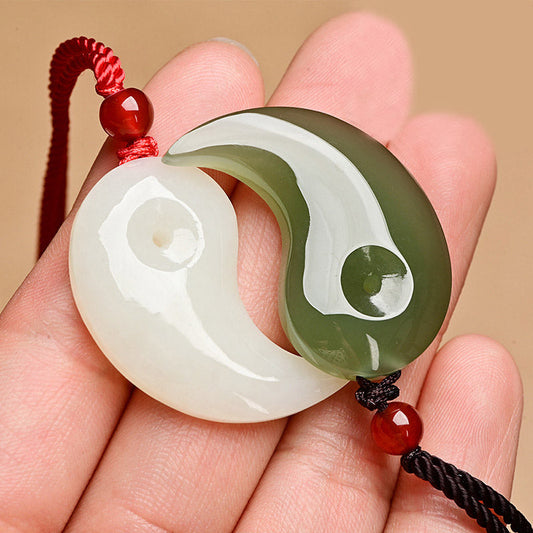 Yin Yang Jade Necklace – White and green interlocking jade pendant with red and black cords, held in hand