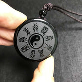 Yin Yang Pendant – hand holding obsidian Bagua disc with trigram symbols and black cord