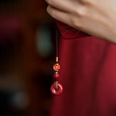 Woman wearing natural cinnabar zodiac amulet phone charm with red peace buckle pendant
