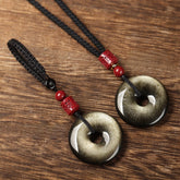 Gold Obsidian Pendant – Two gold sheen obsidian peace buttons with black cord and red beads on wood, grounding jewelry