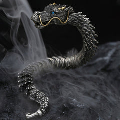 Eastern dragon themed cuff bracelet with oxidized silver scales gold horn accents blue sapphire eye and detailed facial features shown against smoky dark background
