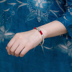 Tibetan Red String Bracelet – worn on wrist over blue floral batik fabric, silver engraved bangle