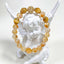Natural Citrine Bracelet – golden yellow and clear citrine beads with gold filigree spacer beads, draped over white angel figurine wings, clean white background, artistic product display