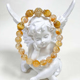 Natural Citrine Bracelet – golden yellow and clear citrine beads with gold filigree spacer beads, draped over white angel figurine wings, clean white background, artistic product display