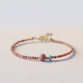 Rhodonite Loving Energy Bracelet – Pink bead bracelet with larger rose focal bead, turquoise accent and gold spacers on white background low side angle
