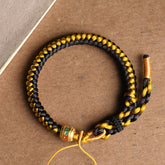 Tibetan Black Gold Dragon Scale Bracelet – overhead flat-lay on kraft paper, braided black and gold cords, handmade bracelet