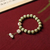 Bodhi Seed Bracelet – Green carved beads with cat paw charm on burgundy fabric beside calligraphy scroll, cat jewelry