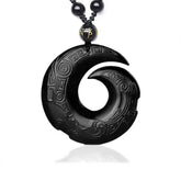 Black Obsidian Ice Obsidian Pendant Necklace – Black polished obsidian spiral carved pendant with intricate Greek key and cloud scroll relief patterns, gold character accent bead, black braided cord, white studio background, obsidian healing crystal jewelry