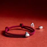 925 Silver Fu Character Braided Bracelet – Red twisted cord bracelet with silver fortune charm and adjustable sliding knot, red textured background flat lay overhead