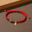 Adjustable red cord bracelet with Hetian jade green bead gold fu blessing fortune charm and sliding knot closure on neutral brown textured background with wooden prop accent
