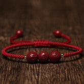 Cinnabar Om Mani Padme Hum Braided Bracelet – Three carved red beads on red cord on wood, cinnabar bracelet
