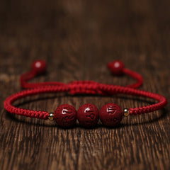 Cinnabar Om Mani Padme Hum Braided Bracelet – Three carved red beads on red cord on wood, cinnabar bracelet