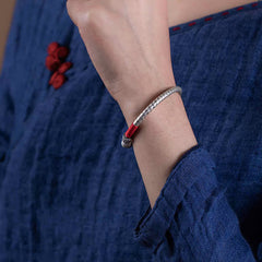 Tibetan Red String Bracelet – worn on wrist with navy fabric and knot button, red cord bangle